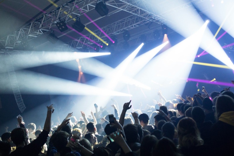 Crowd with raised hands under white stage light beams.