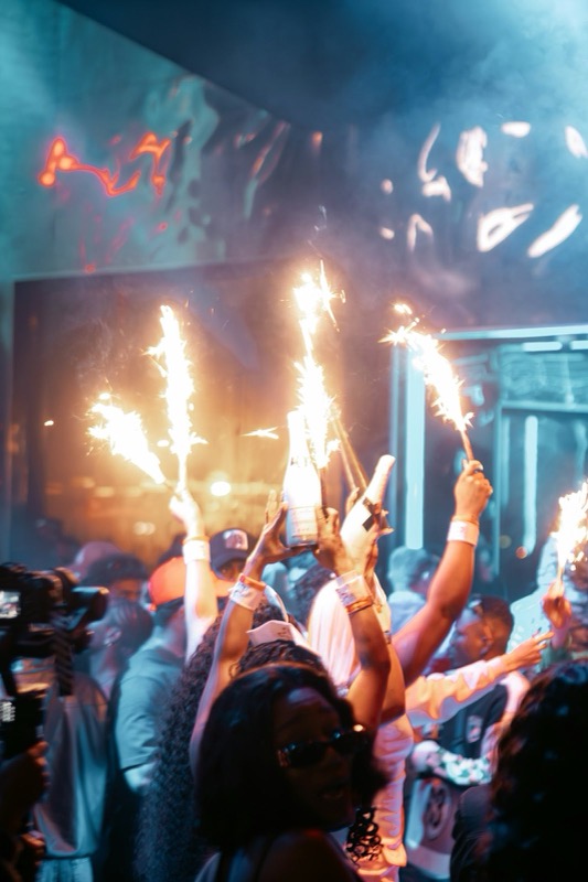 Group holding champagne bottles with sparklers above their heads in a club.
