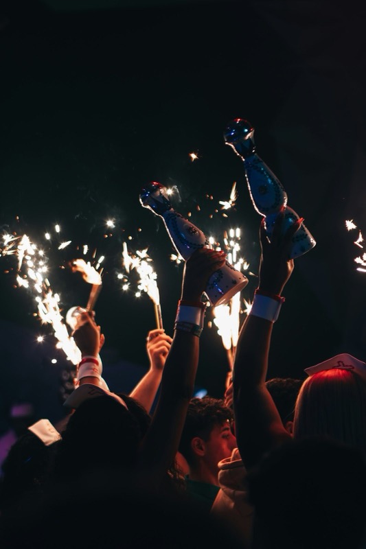Raised hands holding sparkler bottles in the dark.