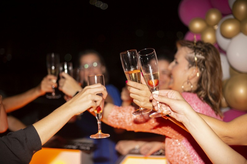 Friends clinking champagne flutes at night, one in pink sequins.